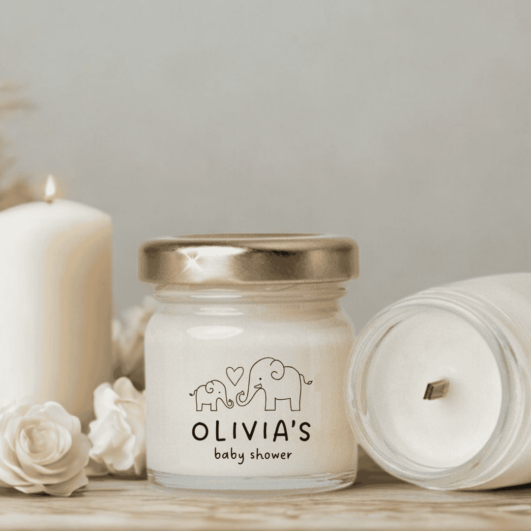 Jar of candle with 'Olivia's baby shower' text and design, surrounded by white flowers and candles on a neutral background.