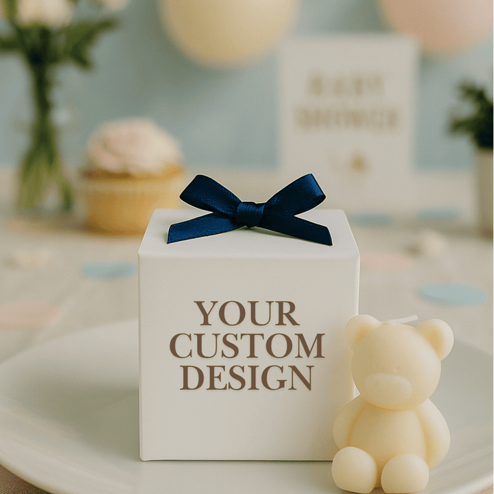 White gift box with a blue bow and 'YOUR CUSTOM DESIGN' text, next to a small teddy bear on a decorative surface.