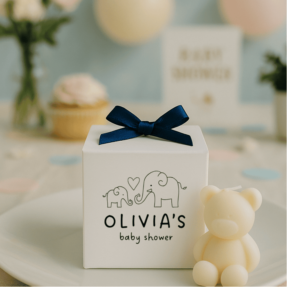 White gift box with navy bow and 'OLIVIA'S baby shower' text, surrounded by decorative items.