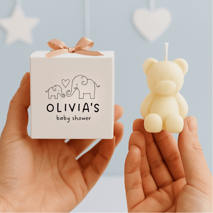 Small white box with 'Olivia's baby shower' text and a bear-shaped candle held by hands against a light blue background.